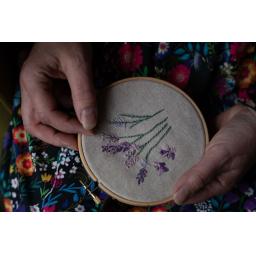 Hand embroidery of purple and pink flowers. Held in hoop against a black and bright coloured flowers