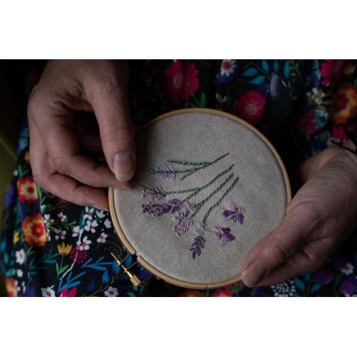 Hand embroidery of purple and pink flowers. Held in hoop against a black and bright coloured flowers